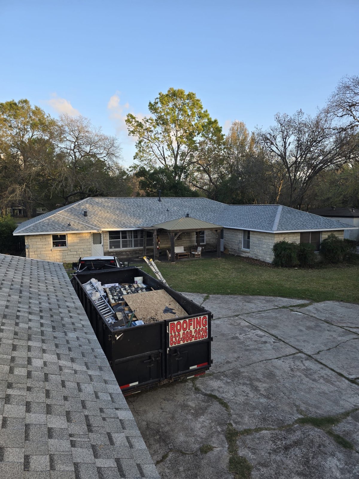 Single-storey house with a newly shingled roof, with a loaded roofing dumpster in the driveway.