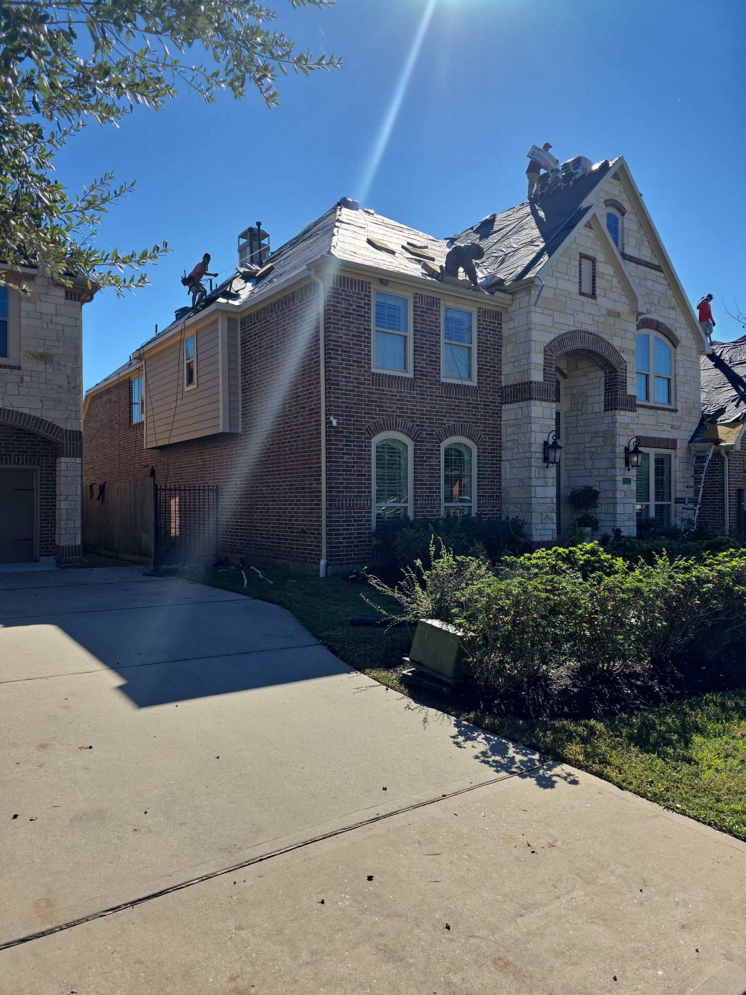 Roofers working across the slopes of a two-storey brick and stone house with underlayment exposed.