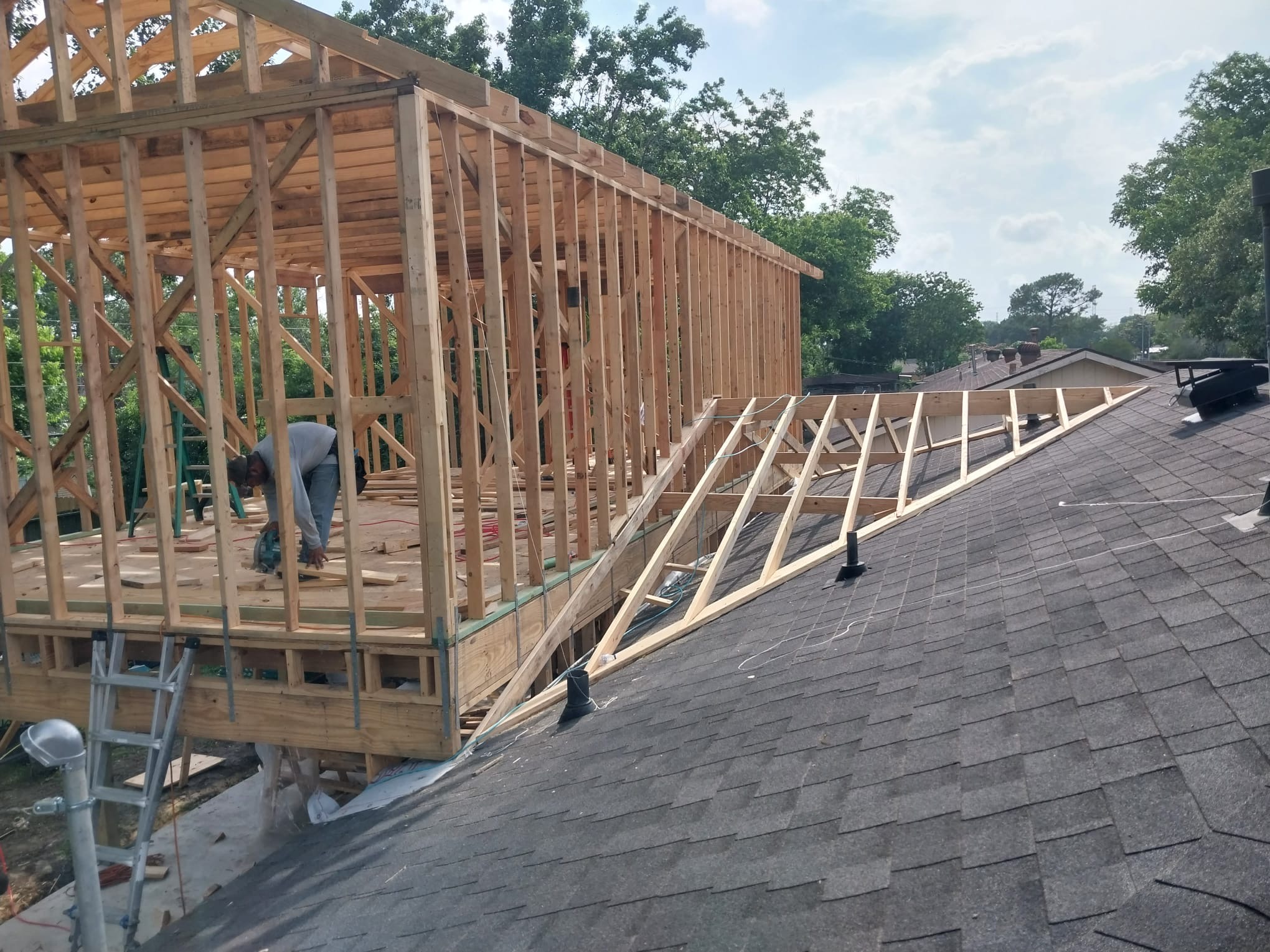 Worker cutting timber inside a new timber-framed addition built above an existing shingle roof.