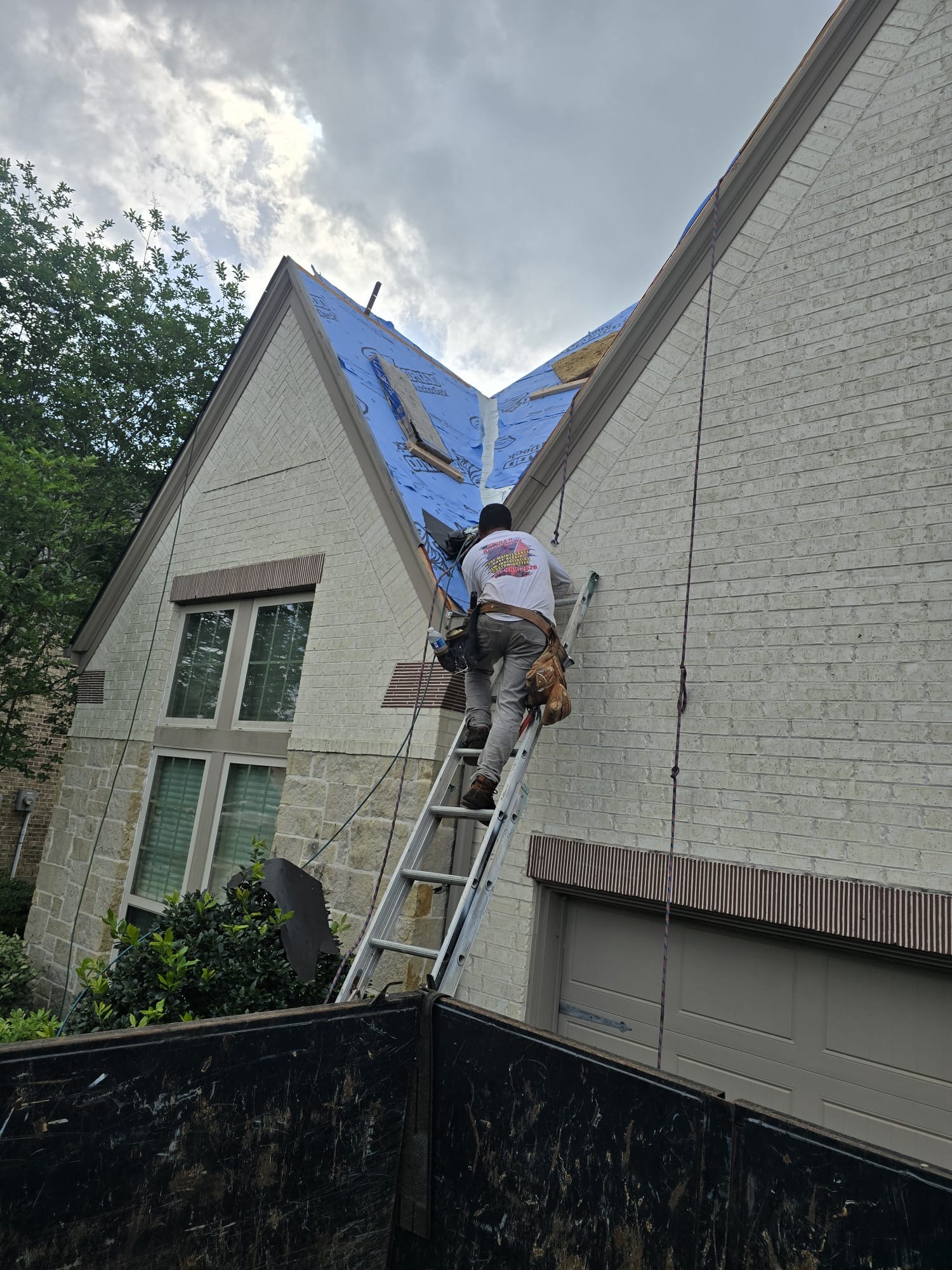 Ladder set against a roof edge with roofing materials stacked on the deck during work.