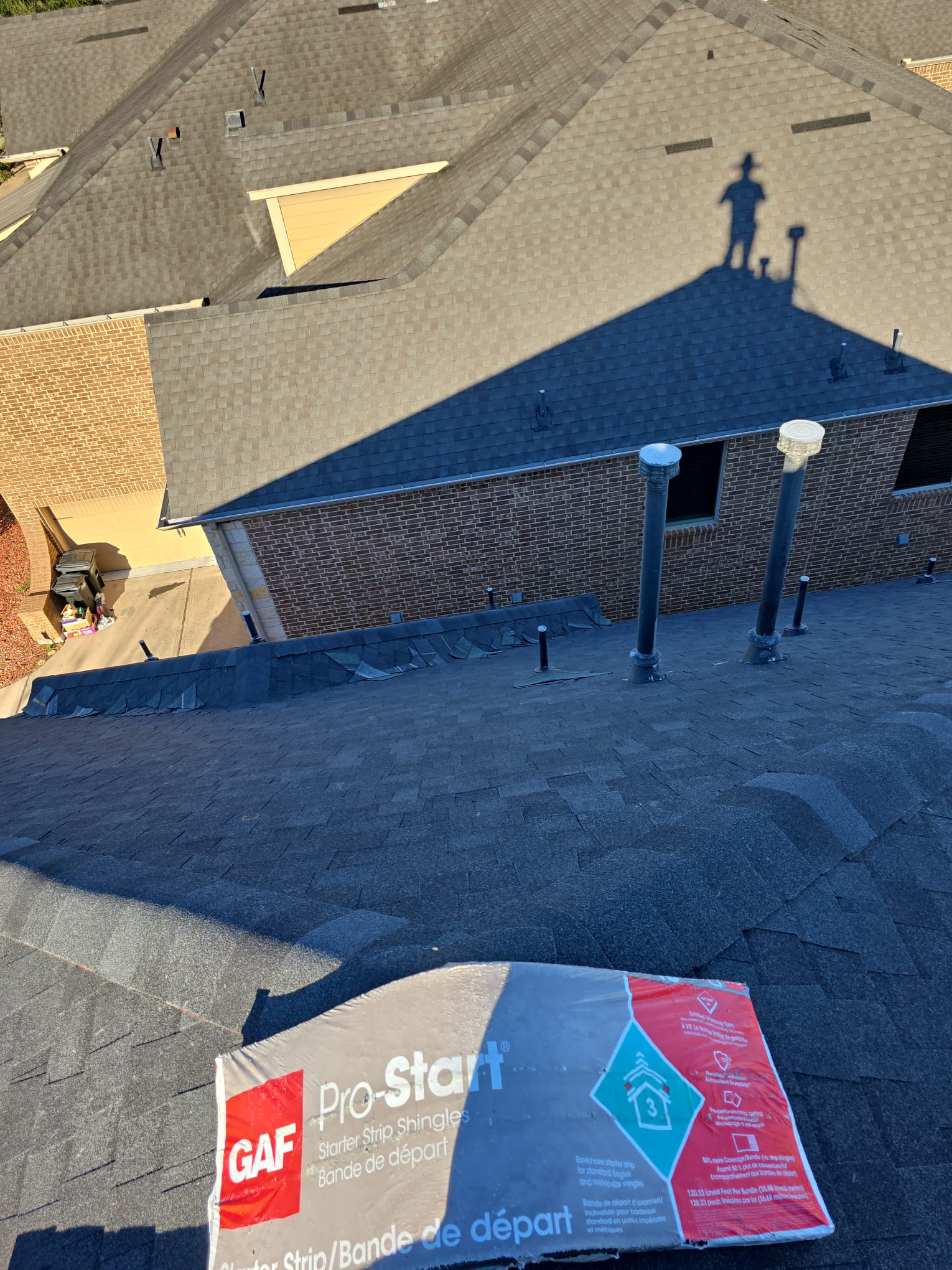 Dark shingle slopes with a bundle of starter strip shingles and pipe vents on the roof.