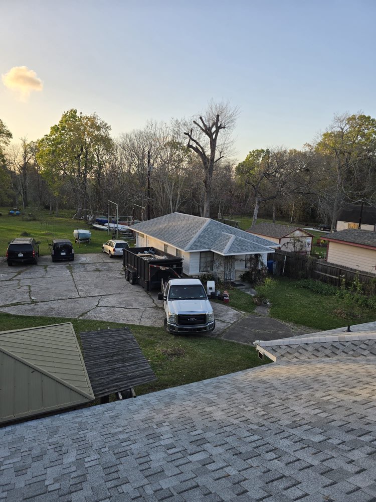 Elevated view from a shingle roof over a neighbouring house, work truck and roofing dumpster.