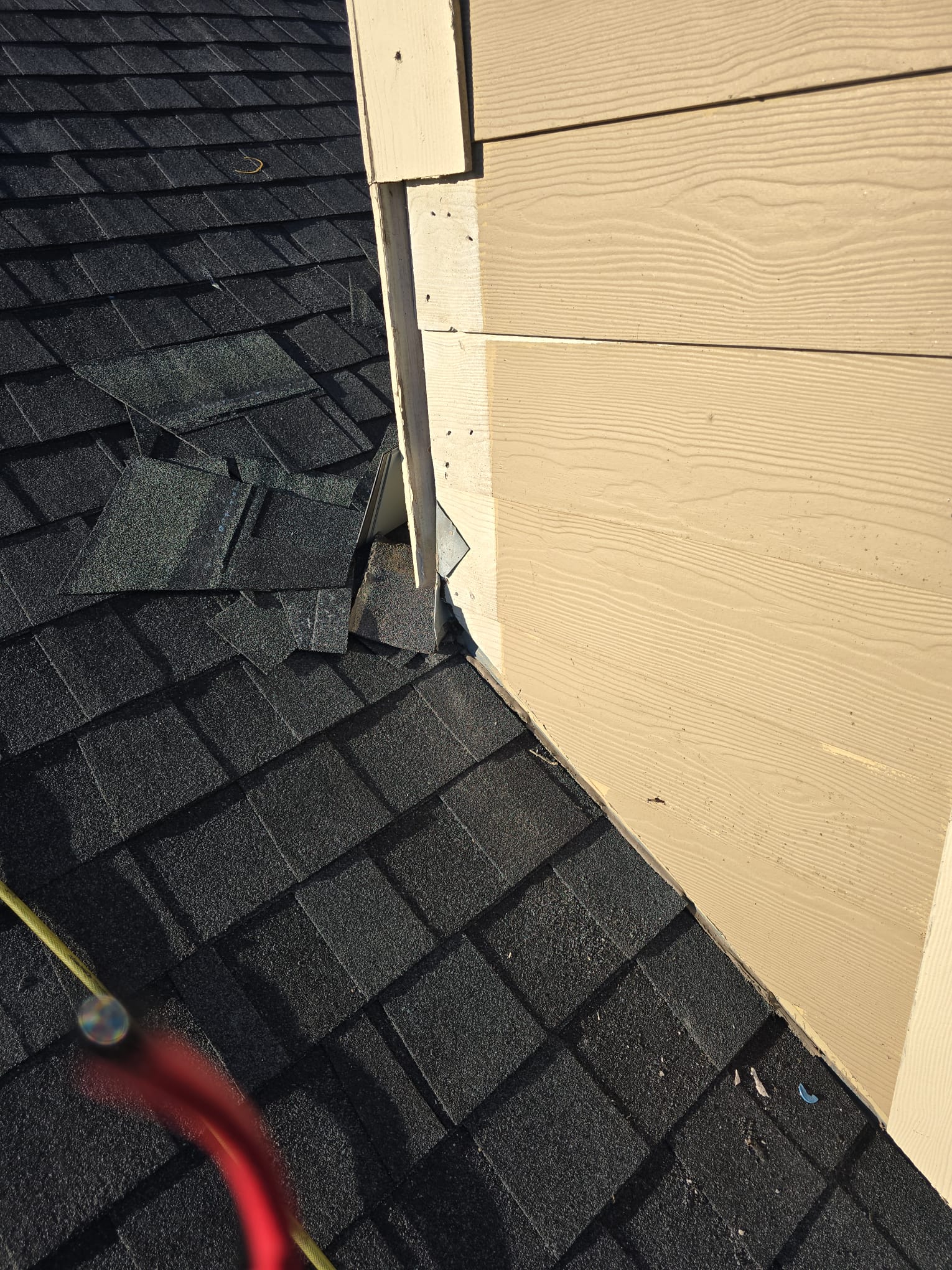 Close view of shingles meeting siding at a wall corner, with step flashing visible.