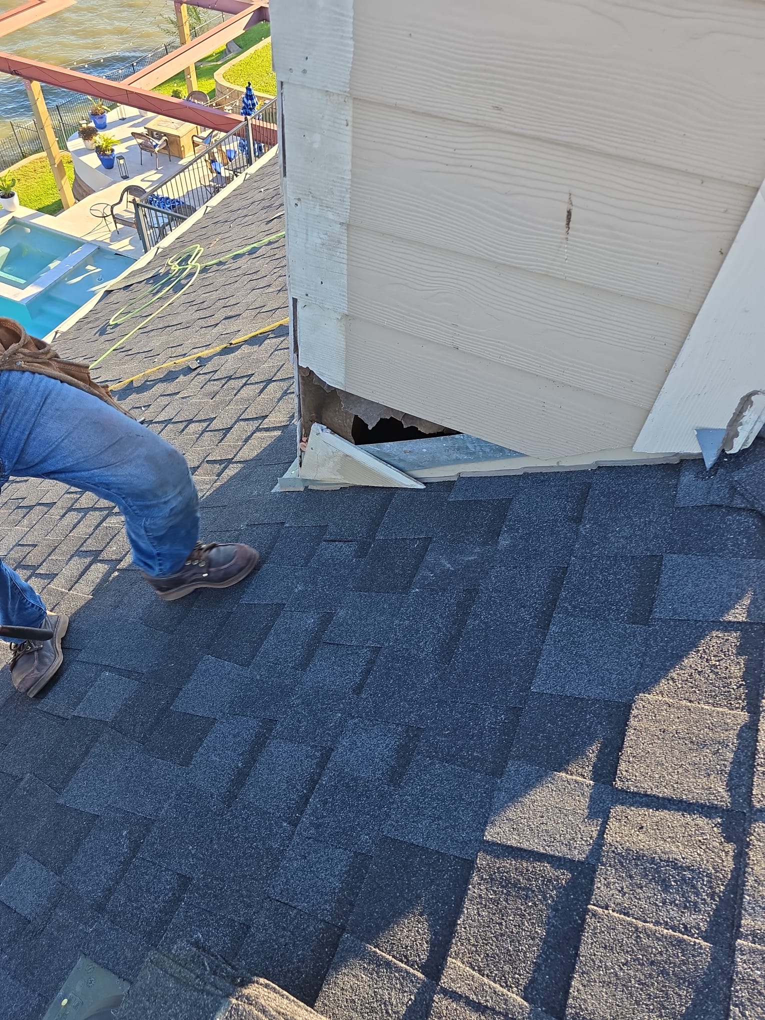 Roofer working at a roof-to-wall junction where the siding is lifted and flashing is exposed.