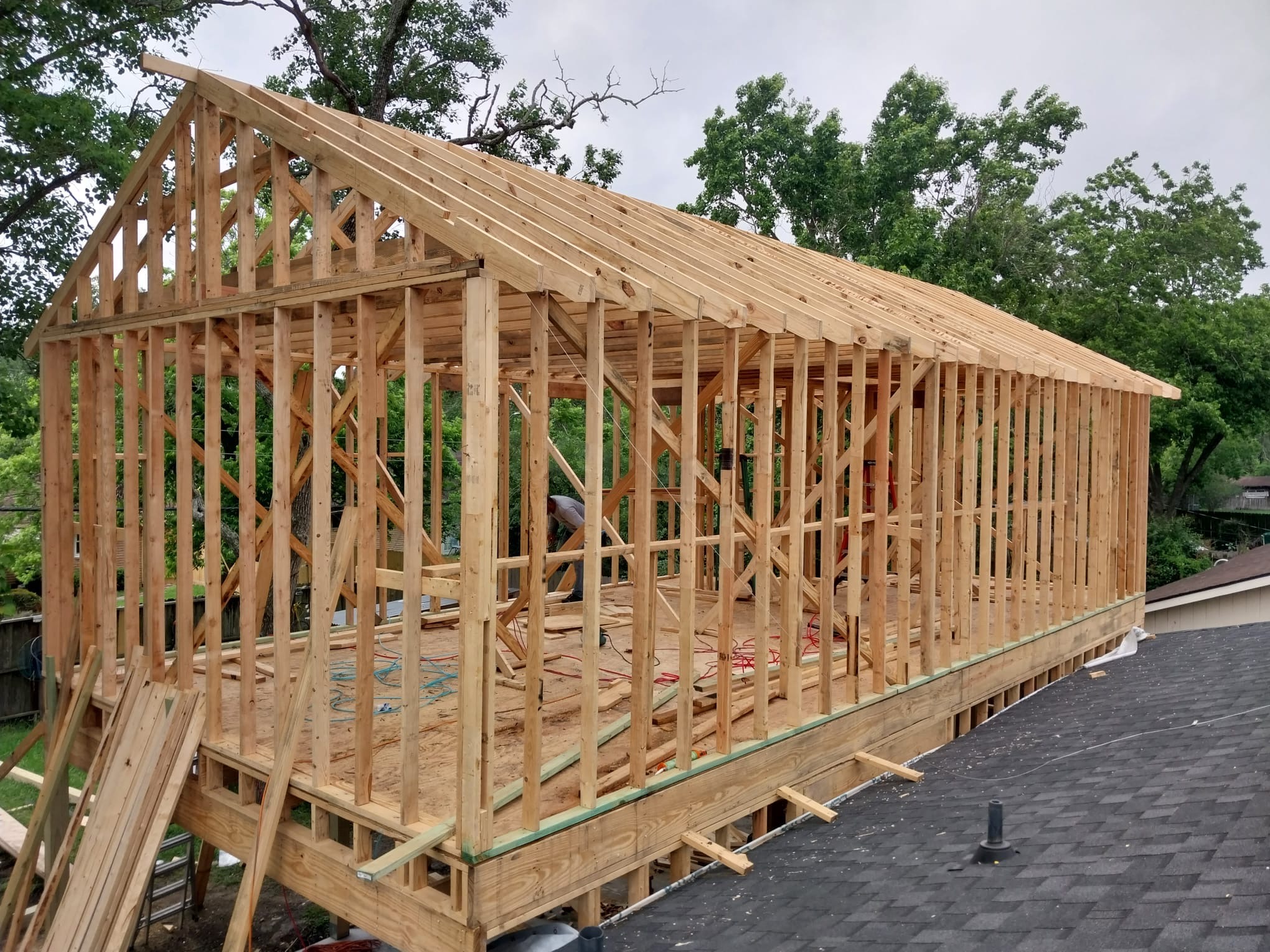Completed timber frame of a room addition standing above an existing shingled roof.